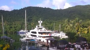 Un yate amarrado en un puerto deportivo con piscina y zona de estar al aire libre, rodeado de exuberante vegetación y colinas.