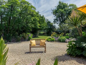 Eine Bank in einem Garten mit Kiesboden, umgeben von verschiedenen Pflanzen und Bäumen.