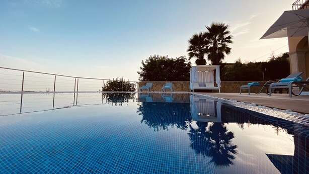 Una piscina infinita azul cristalina con fondo de cristal, rodeada por un muro de piedra y palmeras.
