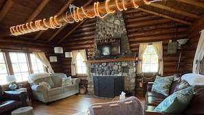 L’intérieur d’une cabane en rondins, avec une cheminée en pierre, des poutres en bois au plafond et un coin salon confortable.