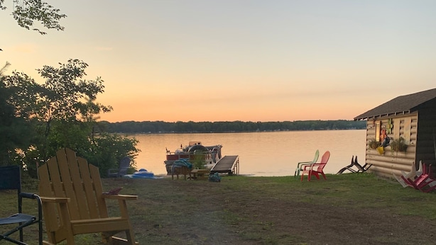 Un foyer circulaire où brûle un feu, entouré d’une pelouse, d’une terrasse en bois et de chaises Adirondack.