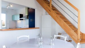 Une cuisine moderne avec un escalier en bois, des meubles blancs et une table à manger ronde entourée de chaises.