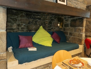 Un muro de piedra, un banco de madera y una mesa con un cruasán y un vaso.