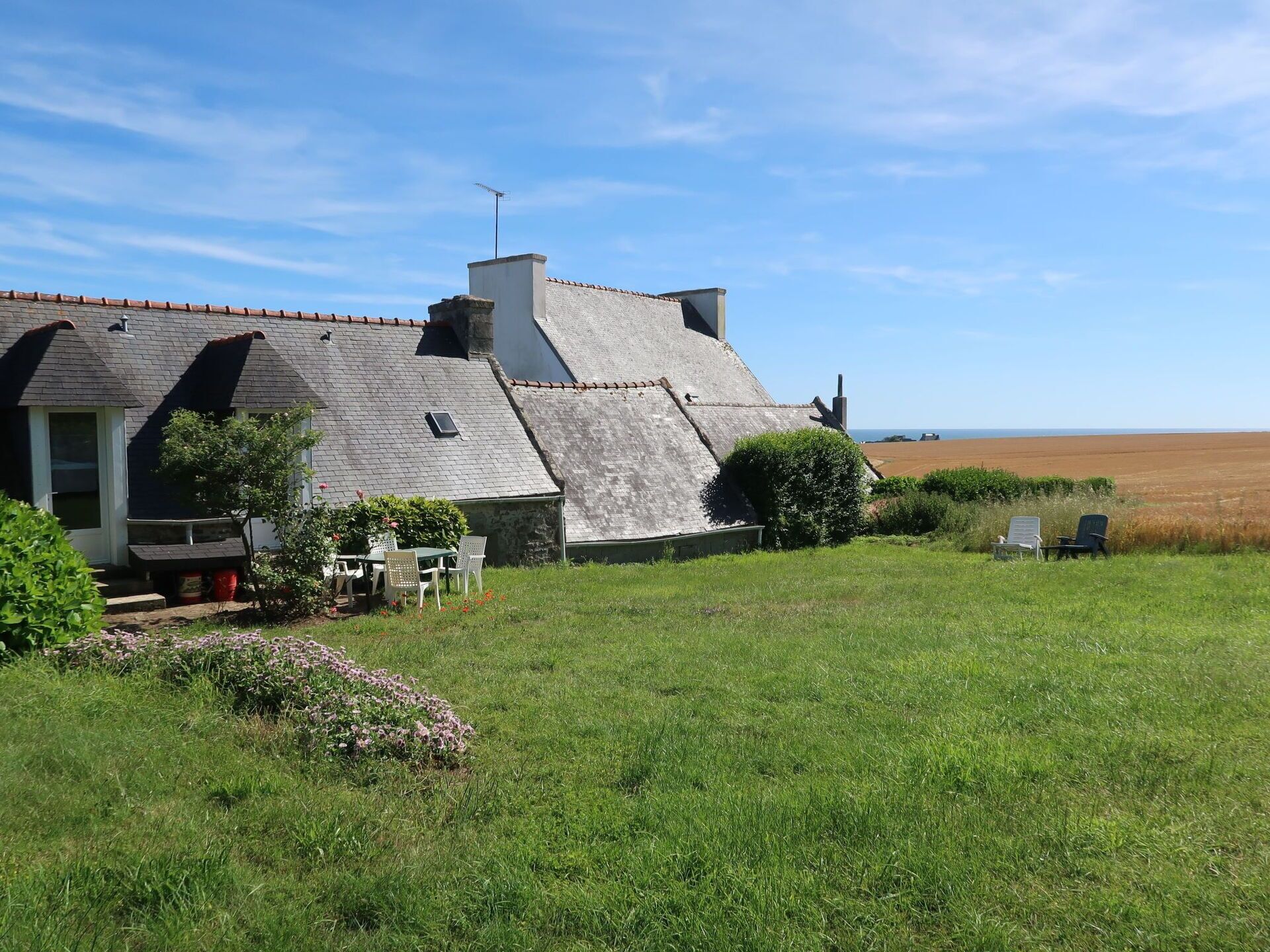 Una casa con tetto spiovente, un camino e un piccolo giardino con tavolo e sedie.