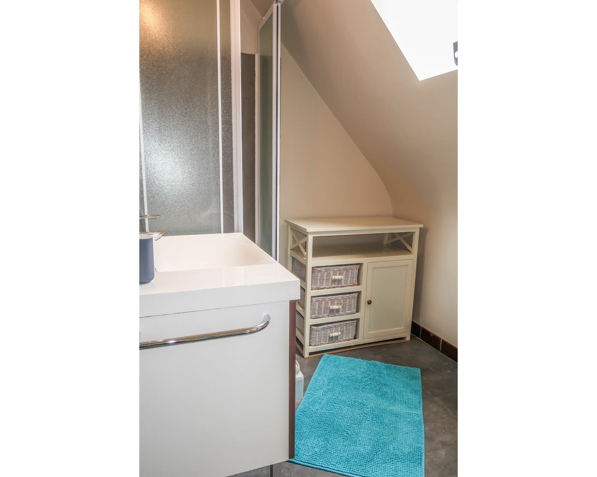 A bathroom with a white sink, a blue bath mat, and a white cabinet with wicker baskets.