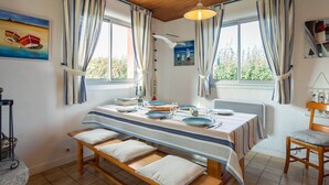 A dining area with a wooden table set for four, benches, and a view of greenery outside. - Beautiful private villa for 6 guests with WIFI, TV, terrace and pets allowed (Saint-Égarec)
