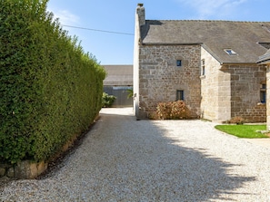 A gravel driveway leading to a stone building with a sloped roof and a small window.