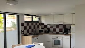 A modern kitchen with white cabinets, a microwave, and a coffee maker. There is a dining table with chairs and a window providing a view of the outside.