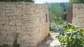 Een stenen muur met een plaquette, een pad en een tuin vol paarse bloemen.