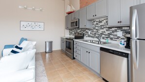 A modern kitchen with grey cabinets, a stainless steel refrigerator, a microwave, and a dishwasher. There is a small sink and a tiled backsplash.