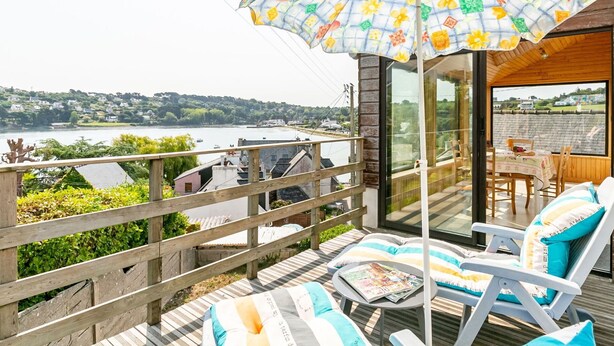 Een terras met lounge stoelen en een tafel, met uitzicht op een meer met boten en huizen in de verte.