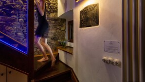 Eine Person geht eine Holztreppe in einem Gebäude mit Steinwänden und einer angebrachten Leuchte hinunter.