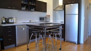 A modern kitchen with dark cabinets, a stainless steel refrigerator, a microwave, and a dishwasher. There are three stools at the island.