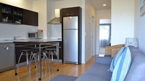 A modern kitchen with a stainless steel refrigerator, a microwave, and a built-in oven. There are bar stools and a grey sofa with striped cushions.