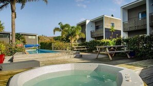 A modern outdoor pool area with a hot tub, wooden deck, and adjacent buildings.