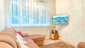 A modern living room with a large window, a flat-screen TV, and a cozy seating area. - ValenciaKV Apartments (Karlovy Vary)