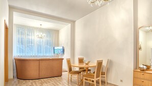A modern living room with a sofa, dining table, chairs, and a TV. - ValenciaKV Apartments (Karlovy Vary)