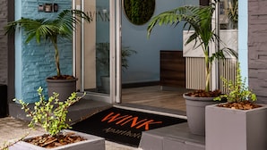Een modern gebouw met een entree, een blauwe muur, grote potplanten en een glazen deur.