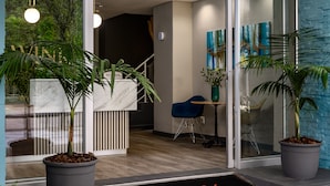 Een modern interieur met een receptiebalie, potplanten, een blauwe stoel en een glazen deur die leidt naar een trap.