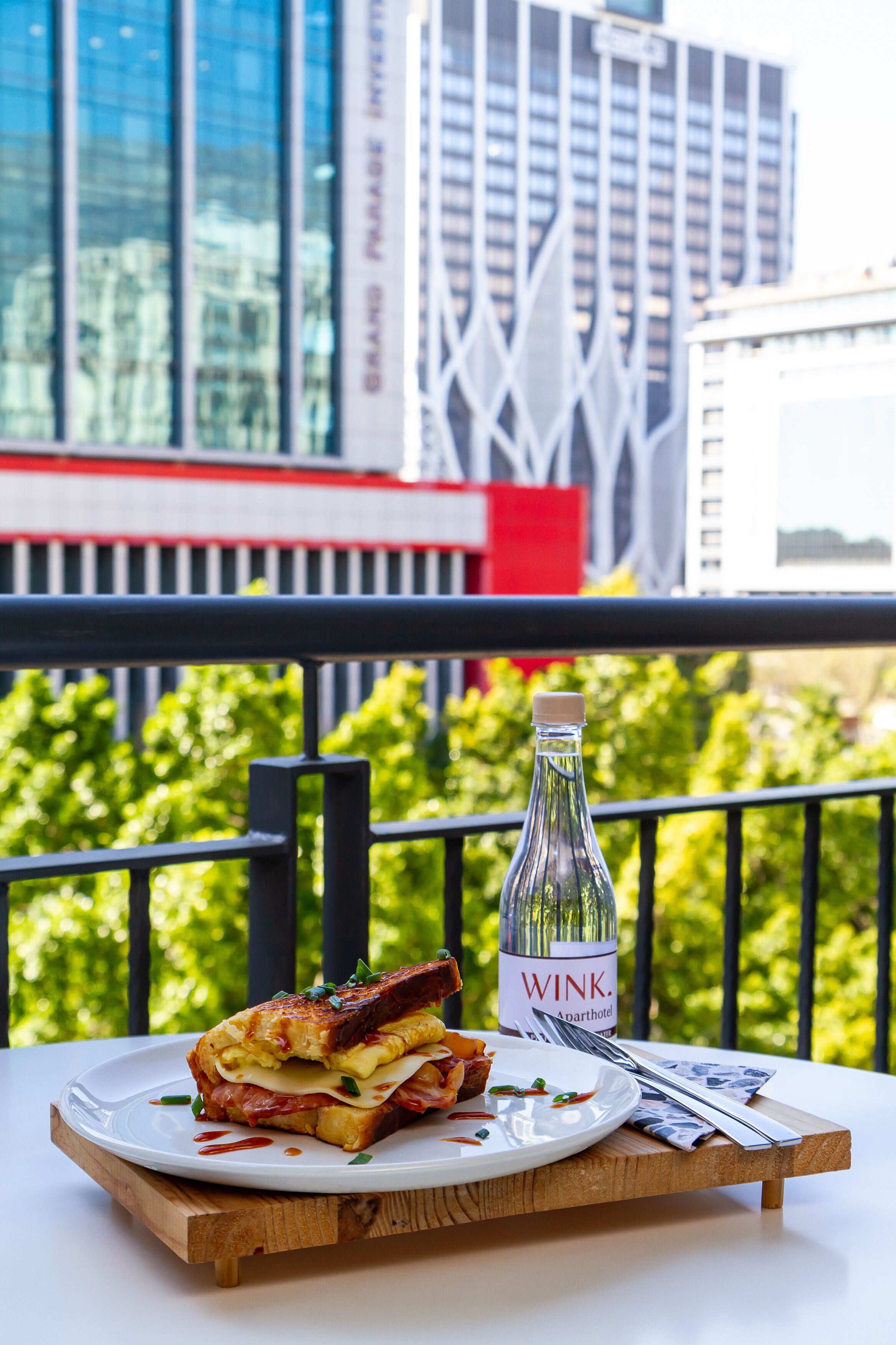 Un sándwich en un plato con una botella de WINK wine, sobre un balcón con vista a la ciudad.