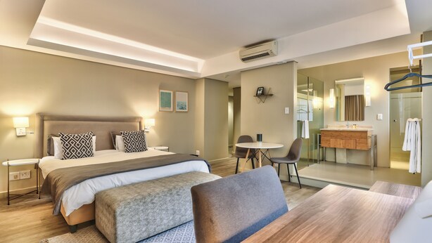 Een moderne hotelkamer met een groot bed, nachtkastjes, een bureau en een badkamer zichtbaar achter een glazen wand.