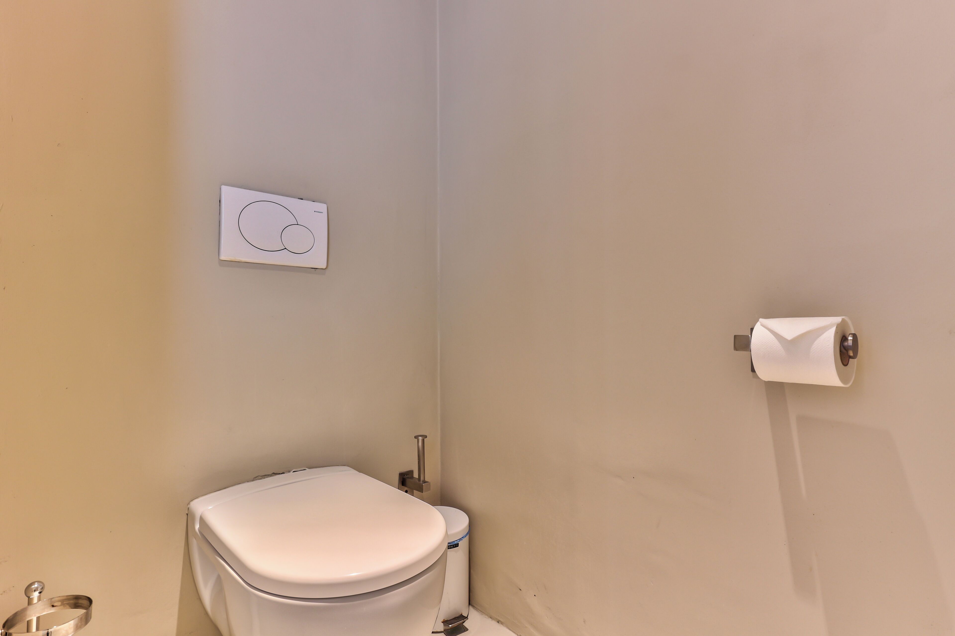 Une petite salle de bain propre, équipée de toilettes, d’un distributeur d’essuie-tout et d’un porte-rouleau de papier toilette fixé au mur.