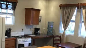 A kitchen with a wooden table, bar stools, a stove, a refrigerator, and a water dispenser.