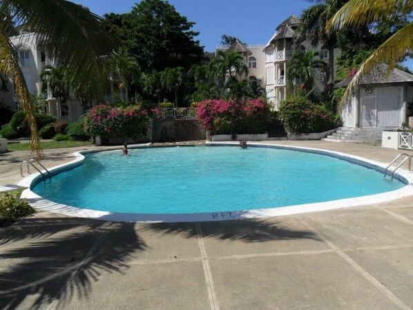 A swimming pool with a 8 FT depth marker, surrounded by lush greenery and palm trees.