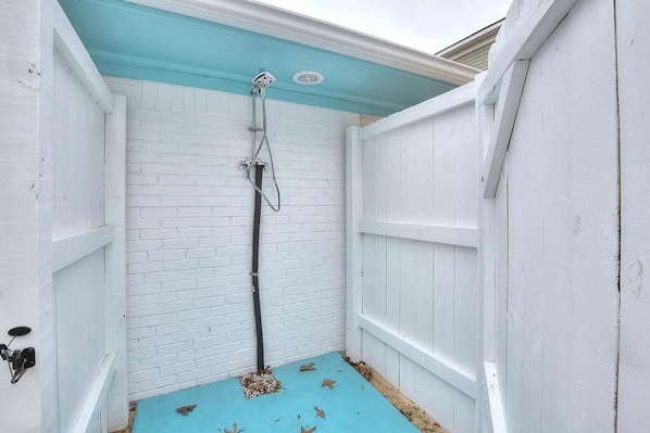 Ein kleiner, abgeschlossener Raum mit einer weißen Backsteinwand, einem blauen Boden und einer weißen Holztür.