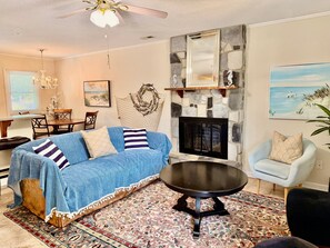 A living room with a blue sofa, a fireplace, a dining area with a table and chairs, and a painting on the wall.