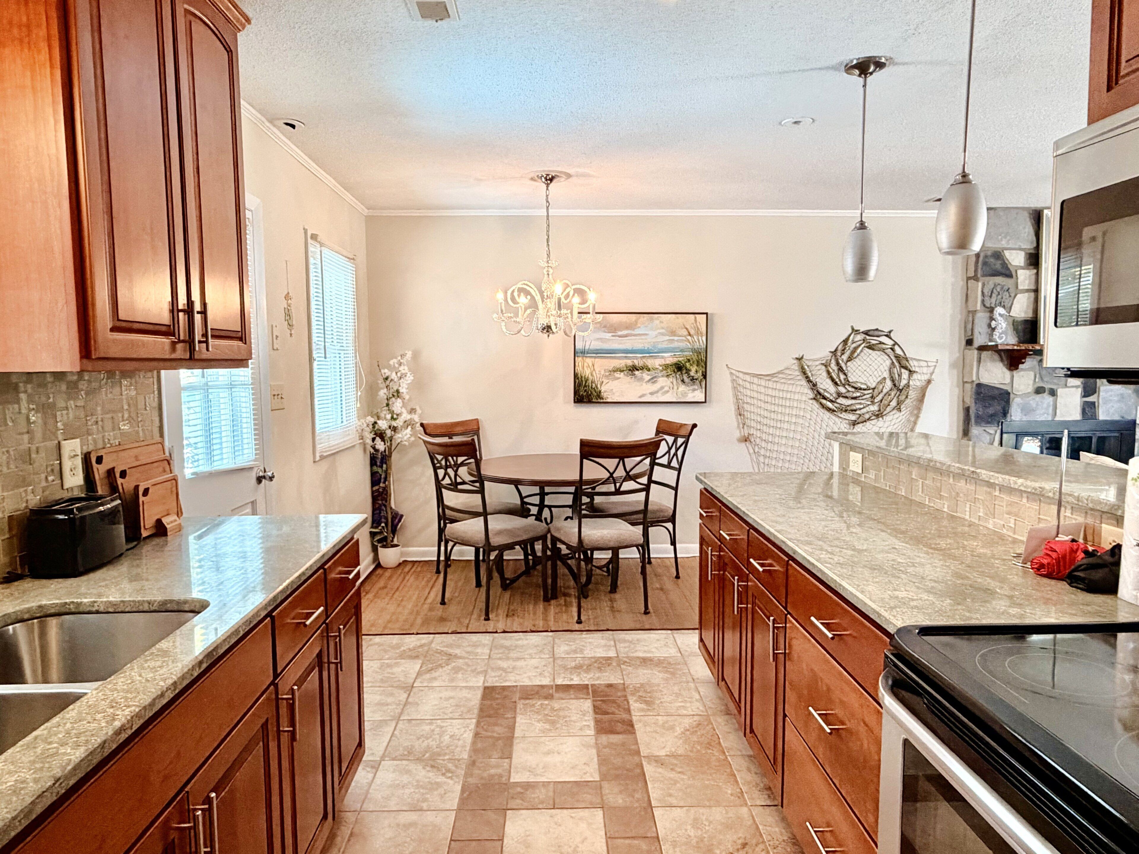 A kitchen with wooden cabinets, a granite countertop, a dining table with chairs, a chandelier, and a stone backsplash.