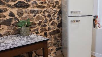 Una pared de piedra, un refrigerador blanco Amica, una mesa de mármol y una planta en maceta.
