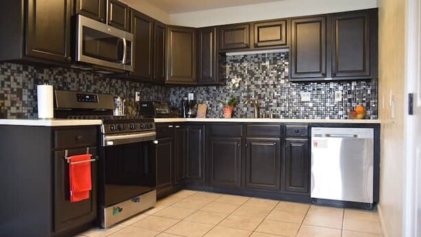 Una cocina con armarios oscuros, microondas, horno, lavavajillas y salpicadero de azulejos.