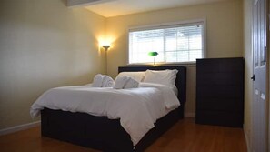 A bedroom with a bed, a nightstand, a lamp, and a window with blinds.