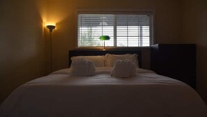 Habitación de hotel con cama, mesita de noche, lámpara y ventana con persianas.