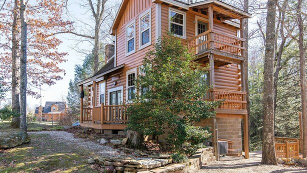 A two-story log cabin with a balcony, surrounded by trees and a stone pathway. - Climber`s Haven- Hot Tub, Firepit, Sunroom, WiFi, 5 mins to Natural Bridge (Rogers)