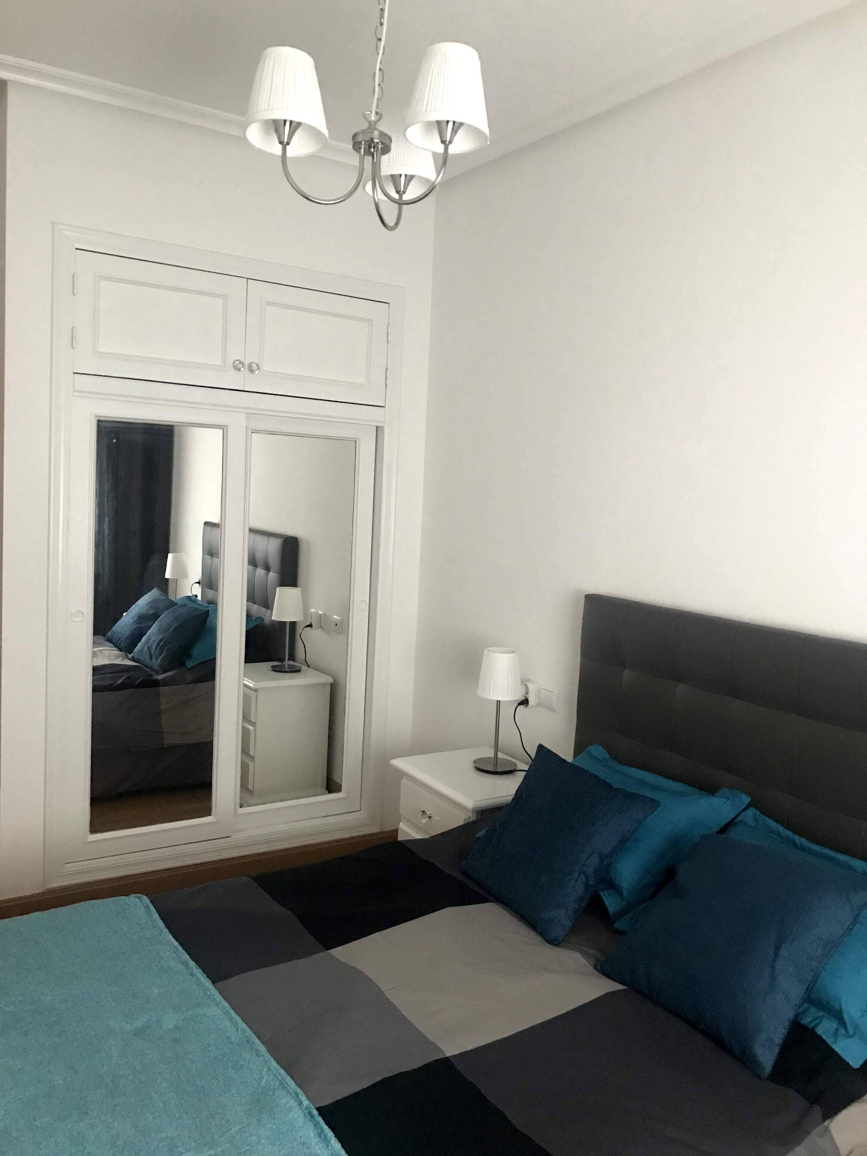A bedroom with a bed, a nightstand, a mirror, and a wardrobe.