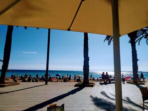 A beachside area with a covered seating area, palm trees, and a view of the sea.