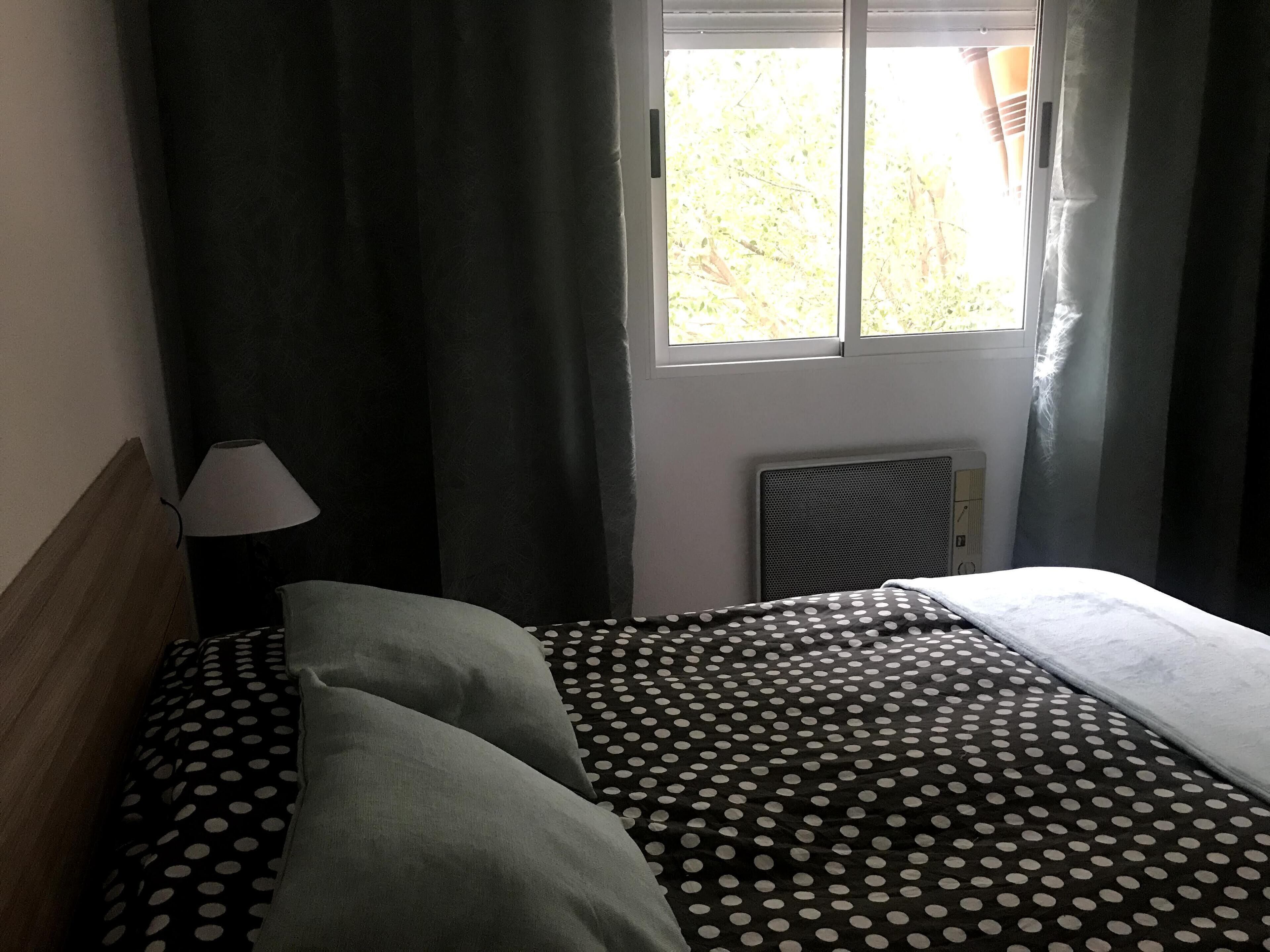 A bedroom with a bed, a nightstand, a lamp, and a window with curtains.