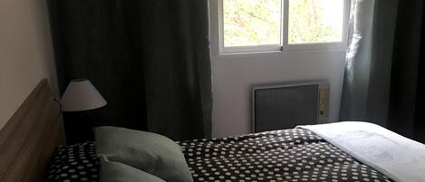 A bedroom with a bed, a nightstand, a lamp, and a window with curtains.