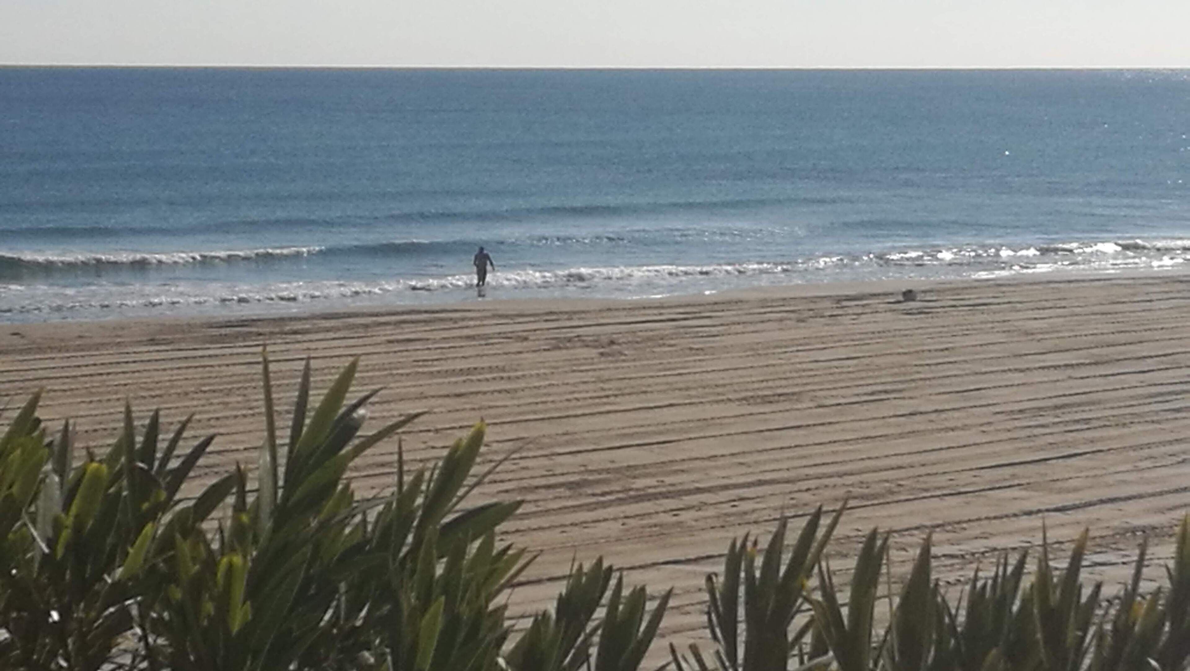 A beach with a person walking, sandy beach, and ocean waves.