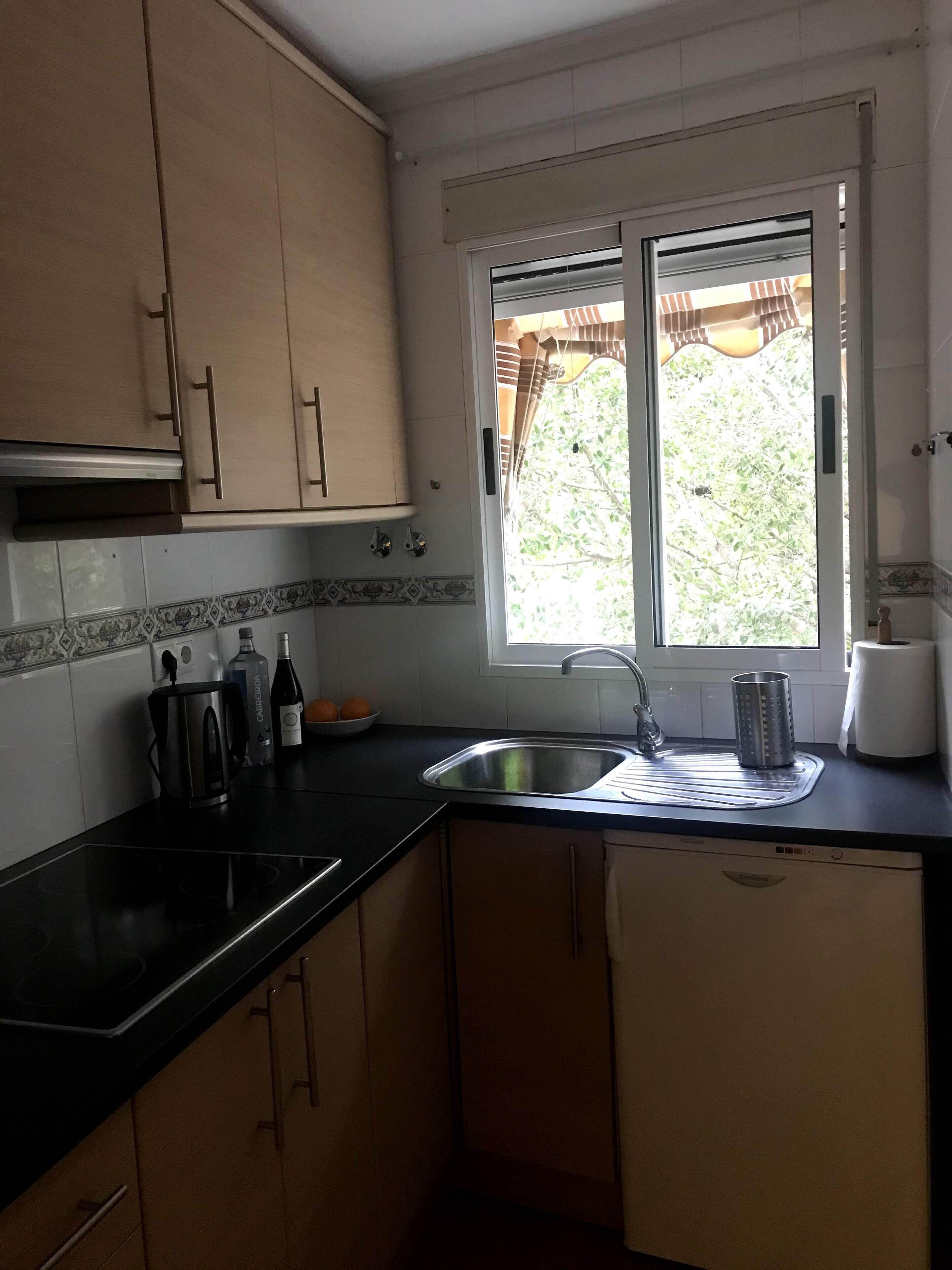 A kitchen with a black countertop, a sink, and cabinets. There is a window with a view of greenery outside.