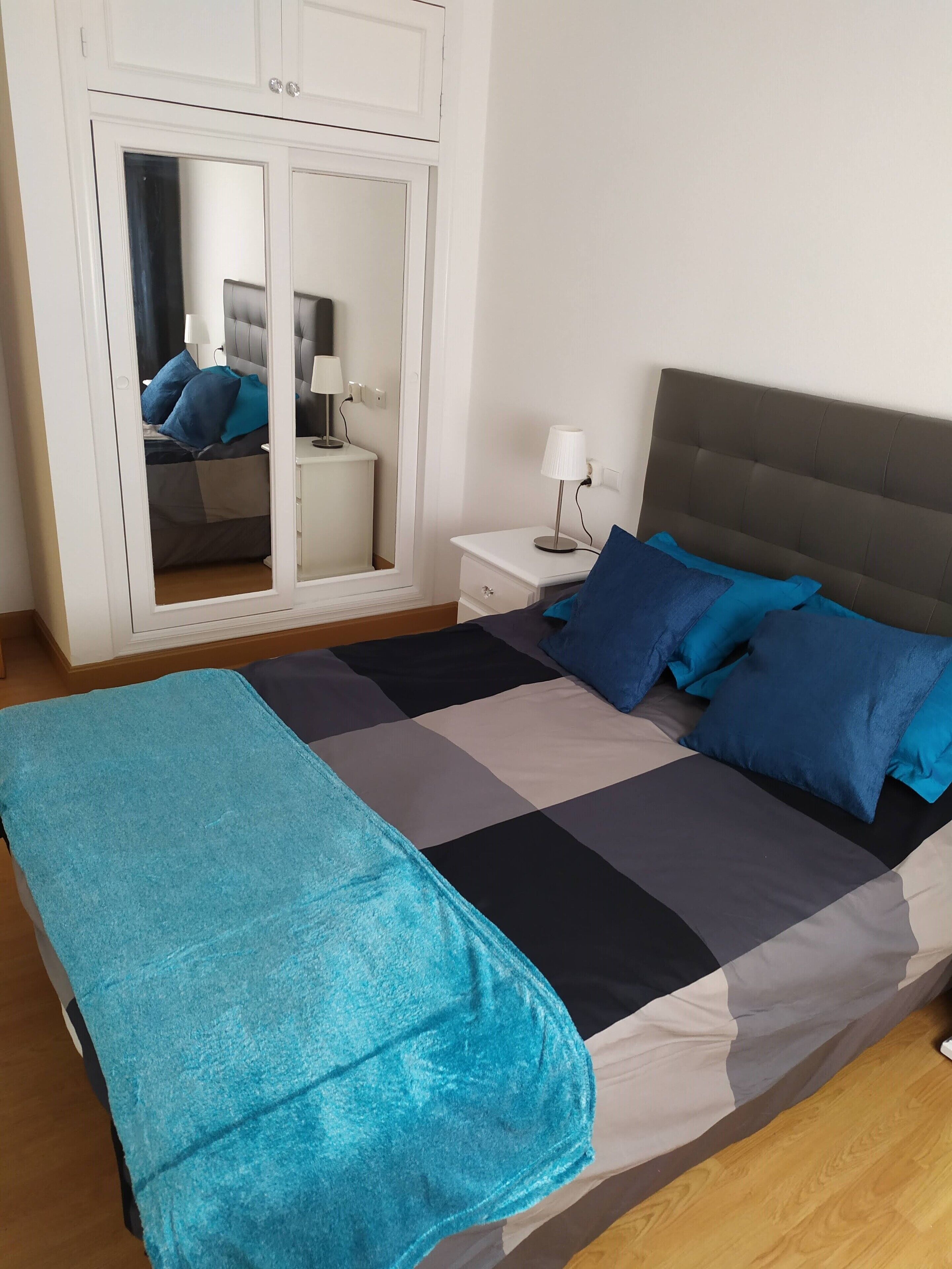 Ein Schlafzimmer mit Bett, Nachttisch, Lampe und einem Schrank mit Spiegel.