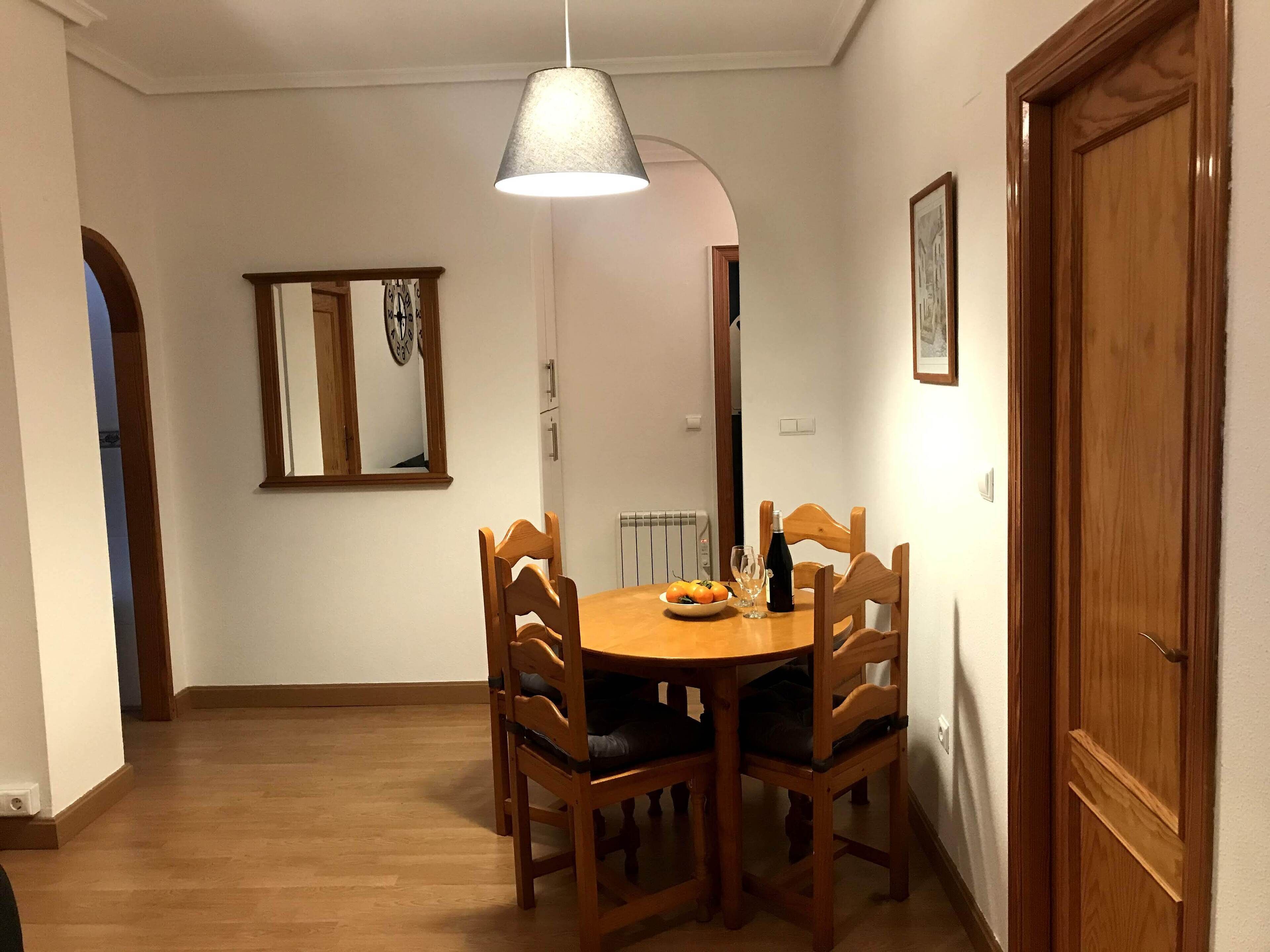 Ein Essbereich mit einem runden Holztisch, vier Stühlen, einer Hängeleuchte und einer Wanduhr.