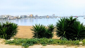 Eine Küstenstadtlandschaft mit einem Yachthafen, Sandstrand und üppiger Bepflanzung im Vordergrund.