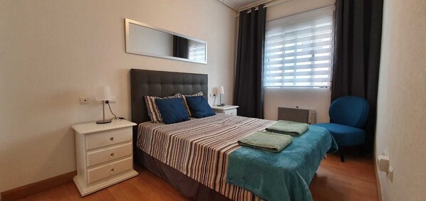 A bedroom with a bed, bedside tables, a chair, a mirror, and a window with curtains.