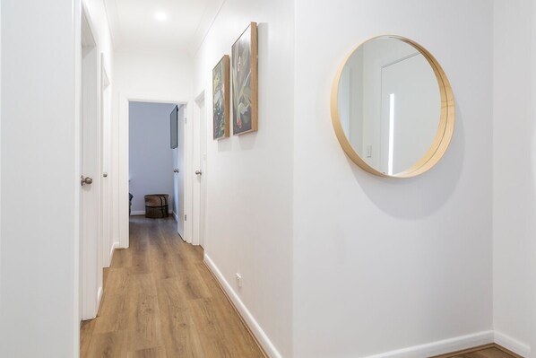 A hallway with wooden flooring, white walls, and a round mirror on the right. - Cook's House @ Tailem Bend (Tailem Bend)