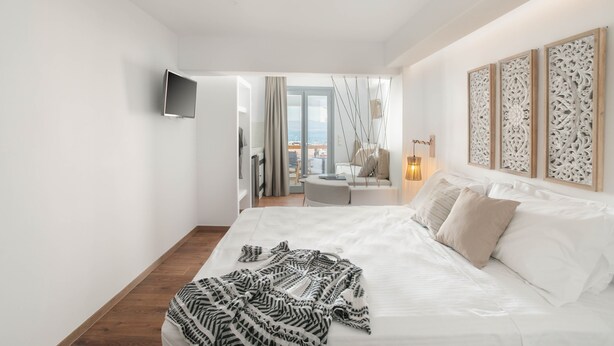 Ein modernes Hotelzimmer mit einem großen Bett, einem flachbildfernseher an der Wand und einem Balkon mit Blick.