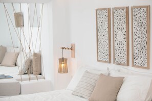 A bedroom with a bed, a hanging light fixture, and three wall-mounted decorative panels. - Kissos Luxury Suites (Naxos)