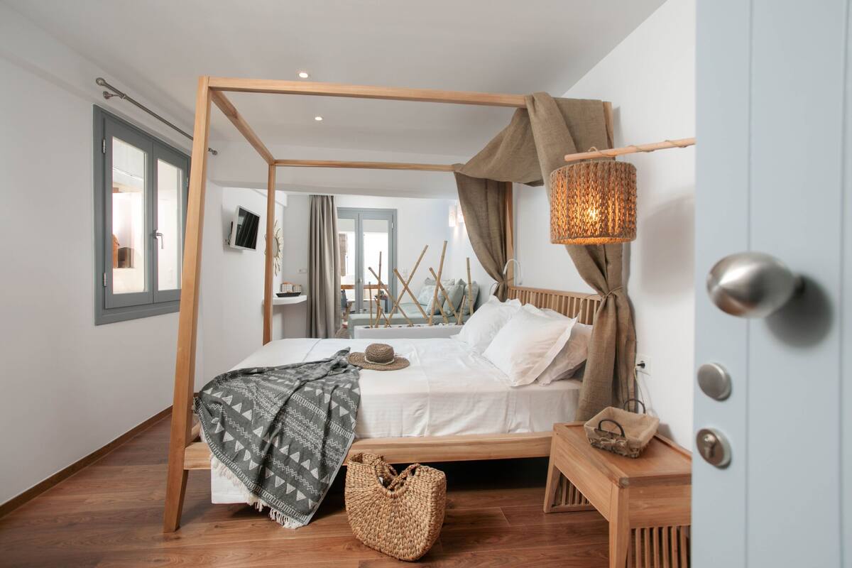 A bedroom with a four-poster bed, a wooden bench, a woven basket, and a wall-mounted TV.